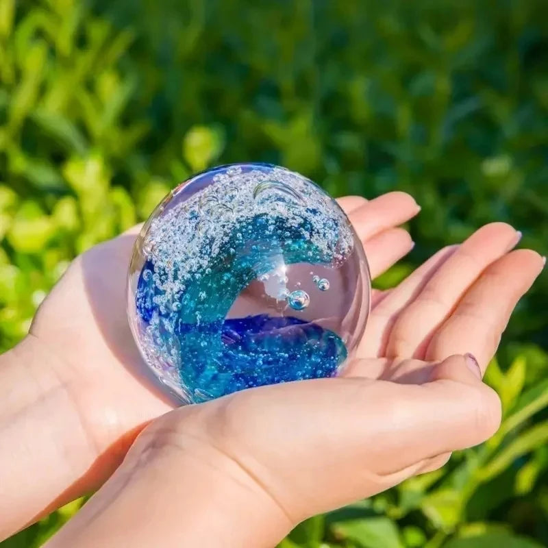 Hand-Blown Ocean Wave Glass Paperweight in natural lighting, accentuating its vivid green and sky blue colors.
