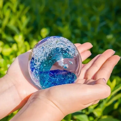 Hand-Blown Ocean Wave Glass Paperweight in natural lighting, accentuating its vivid green and sky blue colors.