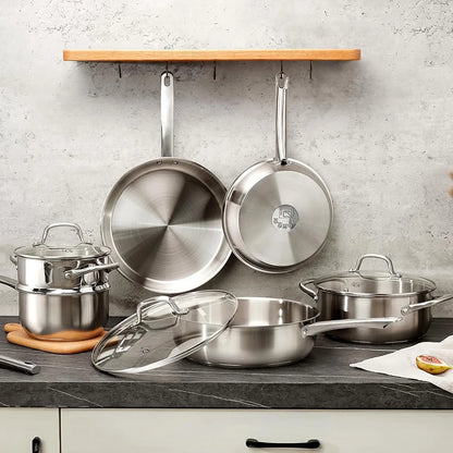 Set of stainless steel cookware on a kitchen counter with a concrete wall background.