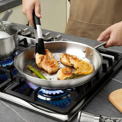 Person cooking chicken and vegetables in a frying pan on a gas stove.