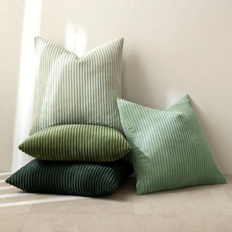 Three striped throw pillows in light sage green, medium sage green, and dark forest green, arranged on a neutral beige floor against a cream wall.