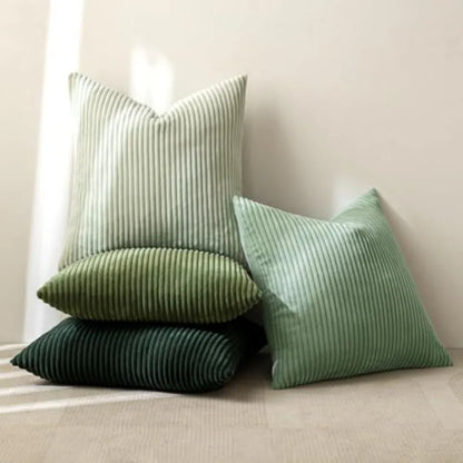 Three striped throw pillows in light sage green, medium sage green, and dark forest green, arranged on a neutral beige floor against a cream wall.