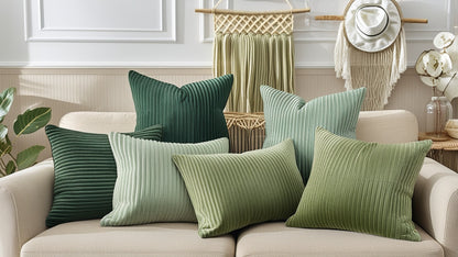 Six textured throw pillows in shades of green and sage are arranged on a beige sofa in a styled living room setting.