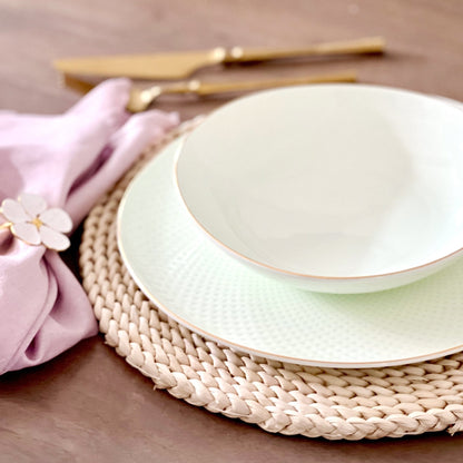 Set of ceramic plates on a woven placemat with gold cutlery and a pink napkin.