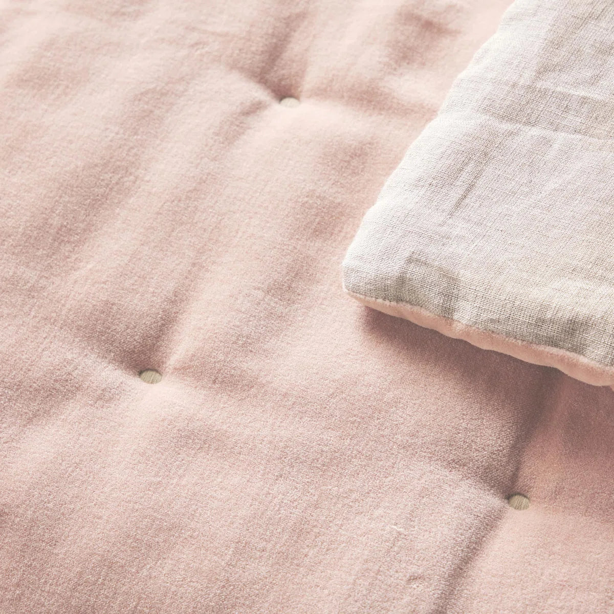 Lifestyle image of the Reversible Luxury Cotton Velvet Throw placed casually on a cottage chair, showcasing its appealing dusky pink color and patterned quilt.