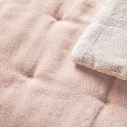 Lifestyle image of the Reversible Luxury Cotton Velvet Throw placed casually on a cottage chair, showcasing its appealing dusky pink color and patterned quilt.
